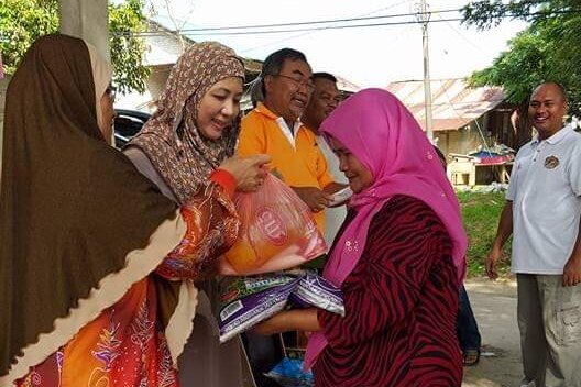 Two women in headscarves handing food out to another woman