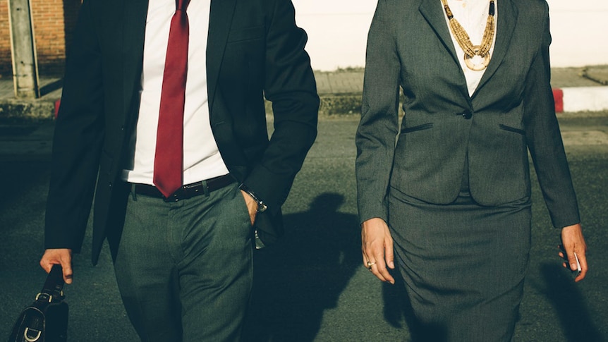 A man and woman dressed in business attire walk together.