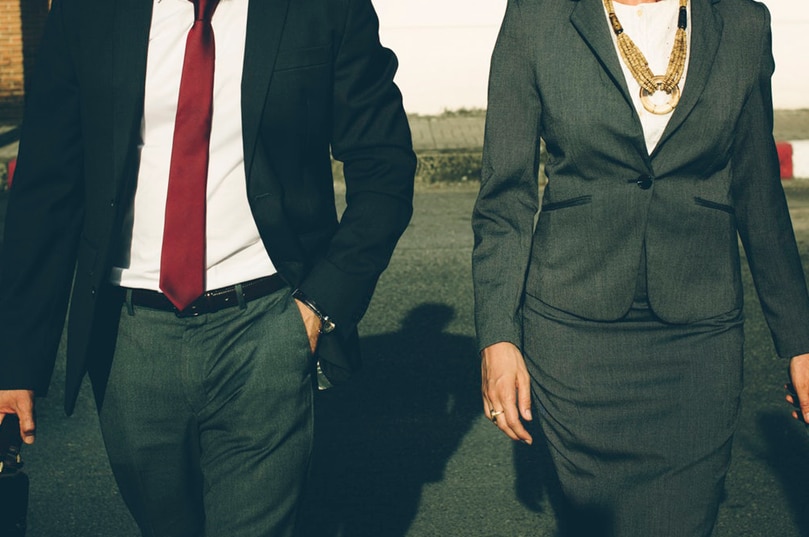 A man and woman dressed in business attire walk together.