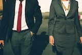 A man and woman dressed in business attire walk together.