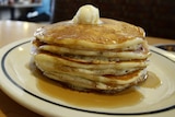 A stack of four pancakes on a plate with ice cream and syrup 