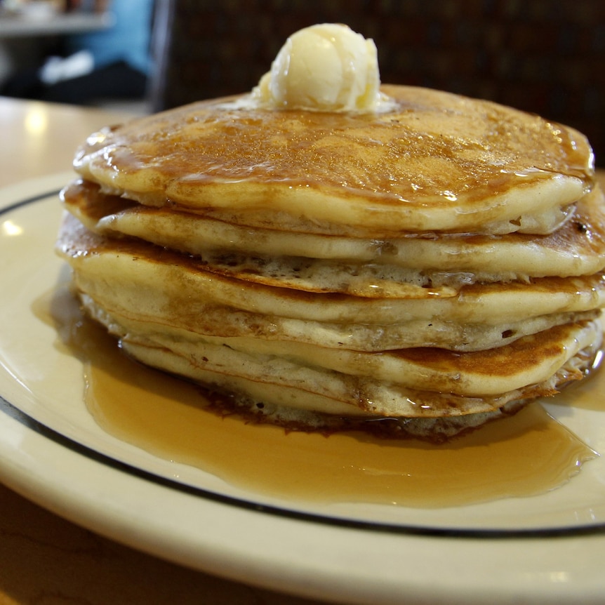 A stack of four pancakes on a plate with ice cream and syrup 