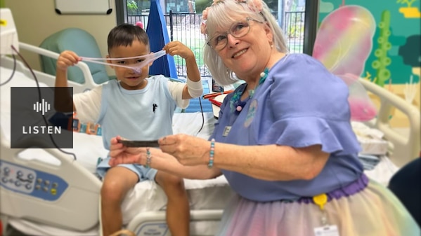 A woman in a fairy costume with a colourful skirt and wings plays with slime with a young boy in a hospital room. Has Audio.