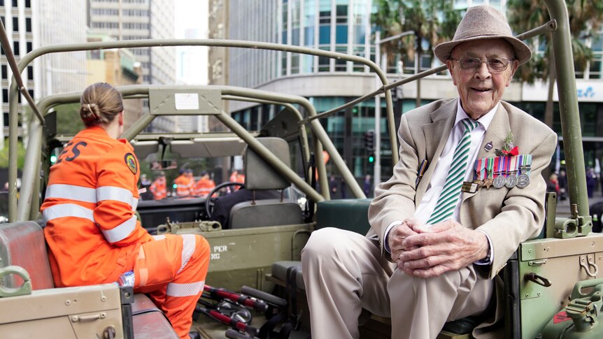 An elderly man decorated in war medals sits on the back of a military truck, ready for the Anzac Day march in Sydney.