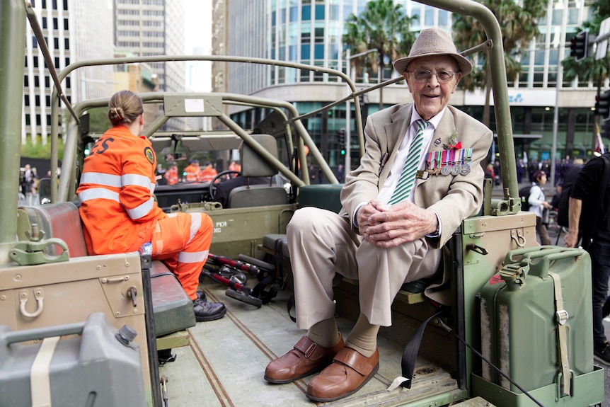 An elderly man decorated in war medals sits on the back of a military truck, ready for the Anzac Day march in Sydney.