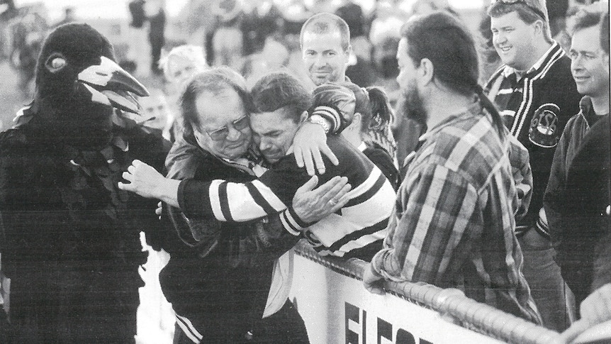 A rugby league coach hugs a fan as the team mascot looks on. 