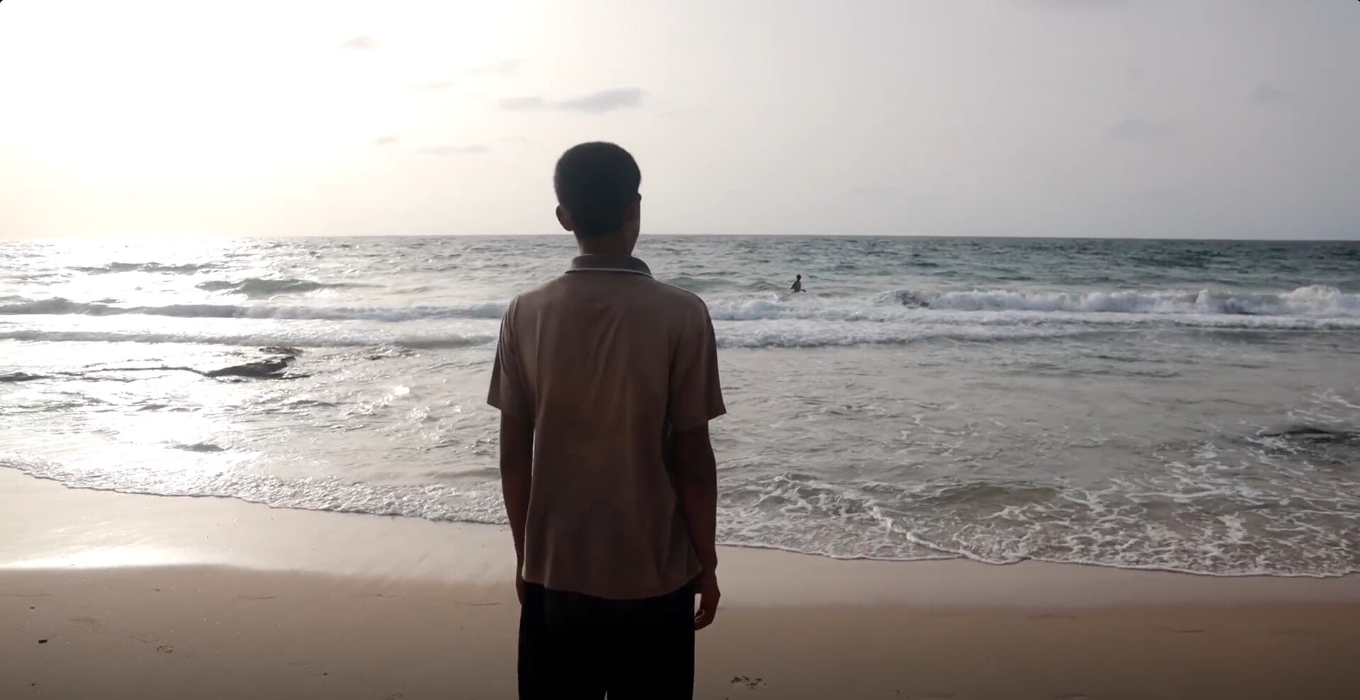 A boy stands looking out at a beach