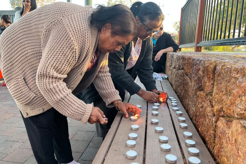 Two Indigenous women light candles at a public memorial. 