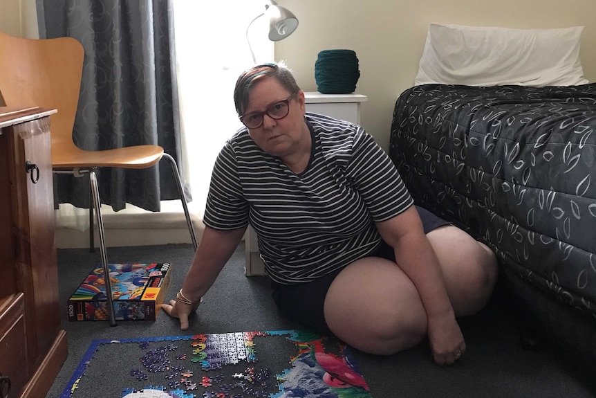 Louise Phillips sits on the floor in a hotel room next to a half completed puzzle.