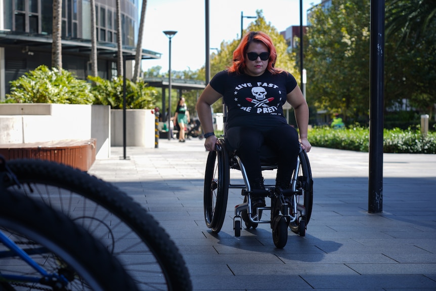 a woman in a wheelchair travelling along the footpath.