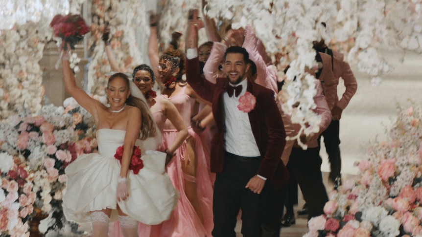 Jennifer Lopez runs down a flower-lined aisle adorned with chandeleirs, flagged by dancers and waving a bouquet.