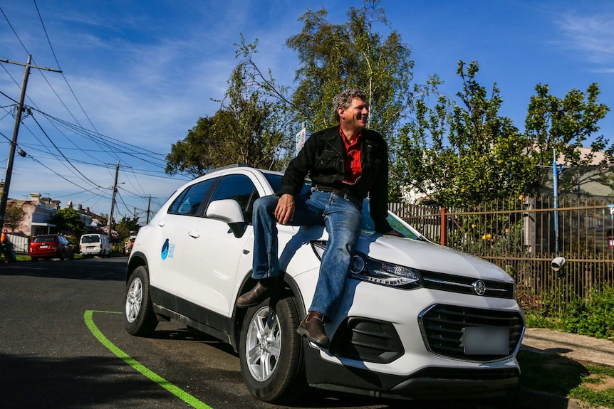 Geoffrey Dunstan sits on the bonnet of his car, which he rents out to others in north Melbourne.