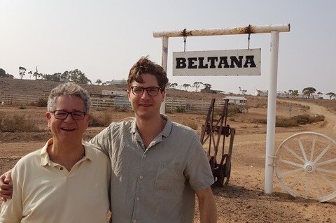 A father and son stand in the outback in front of sign that says "Beltana".