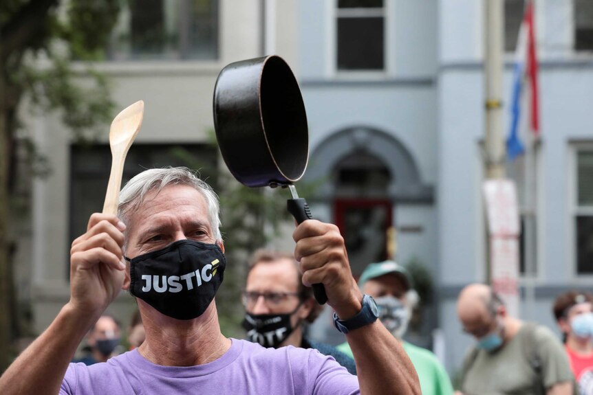 A demonstrator wearing a mask showing the word Justice hits a pot