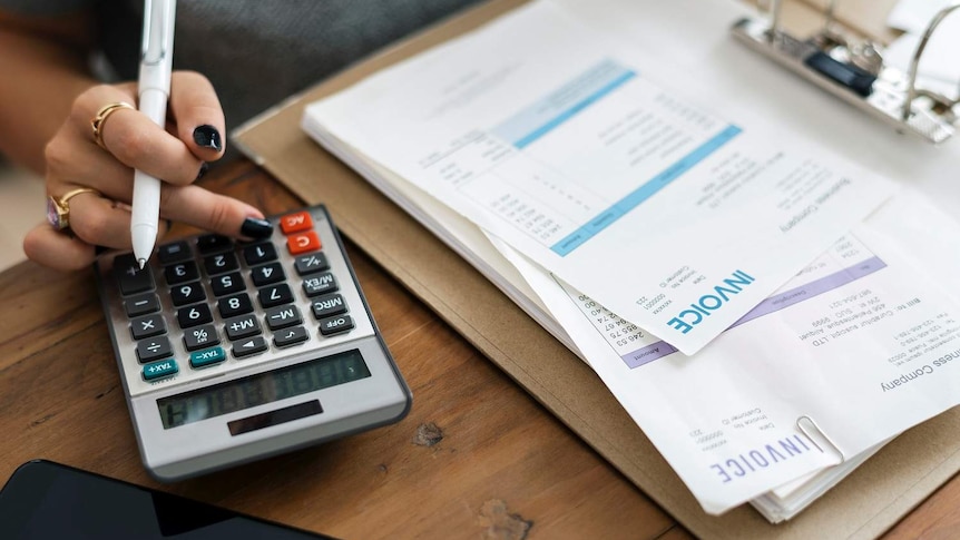 A woman's hand doing calculations with pile of invoices next to her to show ways to get help with debt.