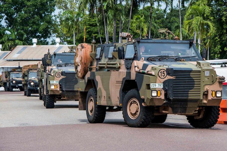 military vehicles are queued in a row with palm trees behind them