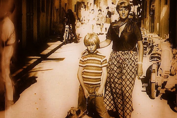 A black and white photo of a woman and her son, who is holding a dog leash, on a busy street in Spain.