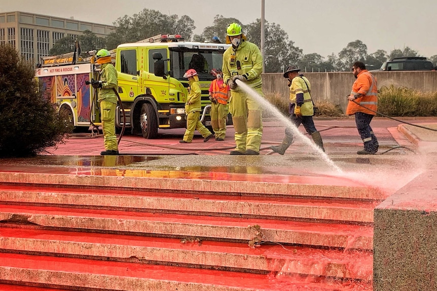 Firefighters hose red retardant from steps.