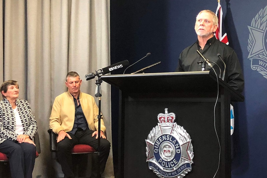 A man speaking to reporters in front of a Queensland police podium