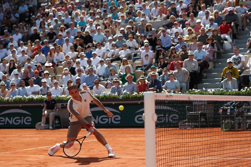 Roger Federer stretches and slides towards the net as banks of spectators watch on