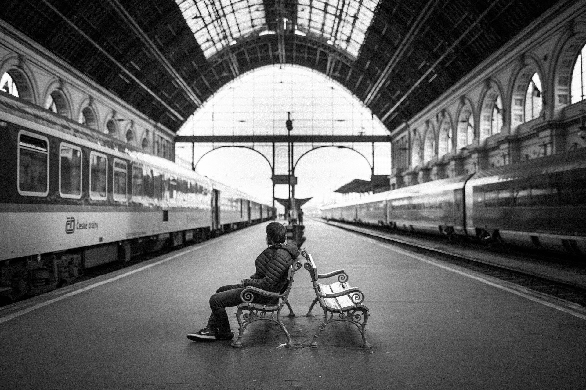 black and white photo - man sits in european train station