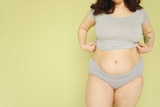 Woman in grey underwear standing in front of yellow background for story on understanding the pelvic floor