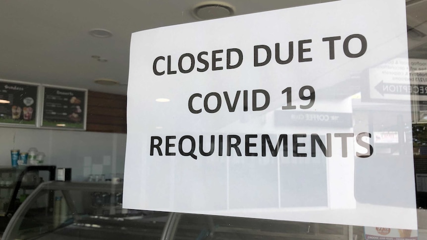 A sign reads closed due to COVID-19 requirements on a shop door.
