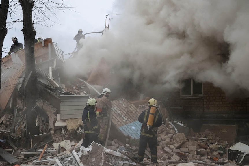 Two firefighters put out a fire in rubble.