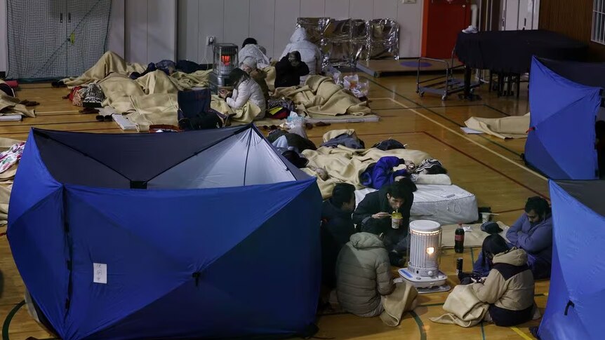 People lie on the floor of an indoor basketball court with blankets