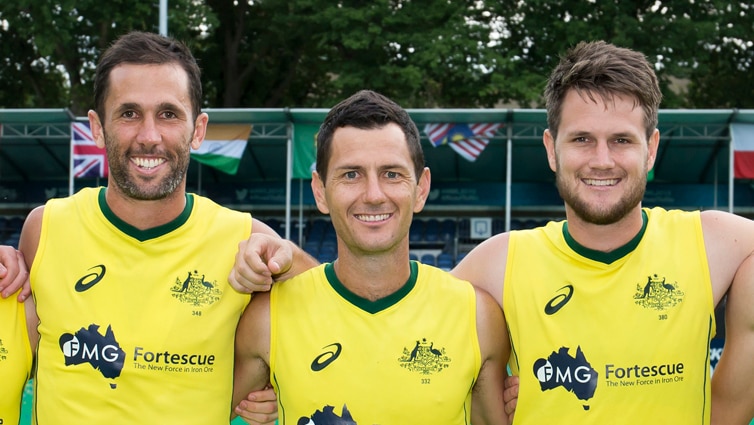 Australian hockey players Mark Knowles, Jamie Dwyer and Matt Gohdes stand on a hockey field with their arms around each other