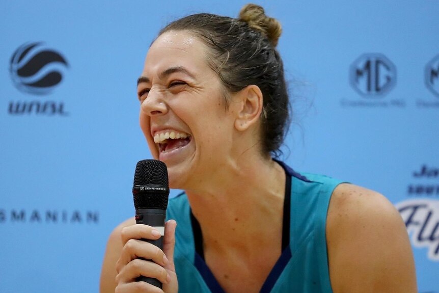 Southside Flyers WNBL player Jenna O'Hea laughs while holding a microphone.