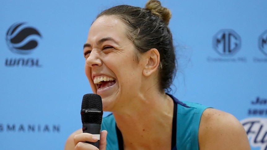 Southside Flyers WNBL player Jenna O'Hea laughs while holding a microphone.