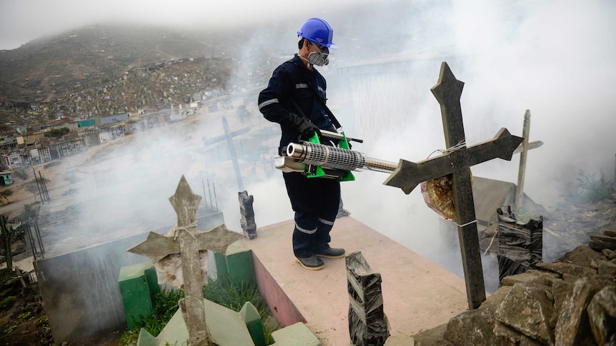 A man wearing protective clothing against Zika virus sprays grave stones with a fumigation machine