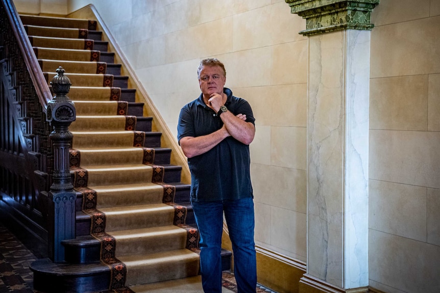 A man stands in front of a federation style staircase.