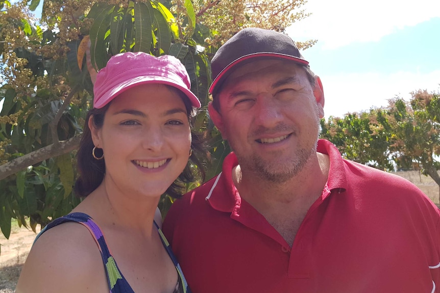 Katrina and Marcello Avolio wearing caps, standing in front of a mango tree