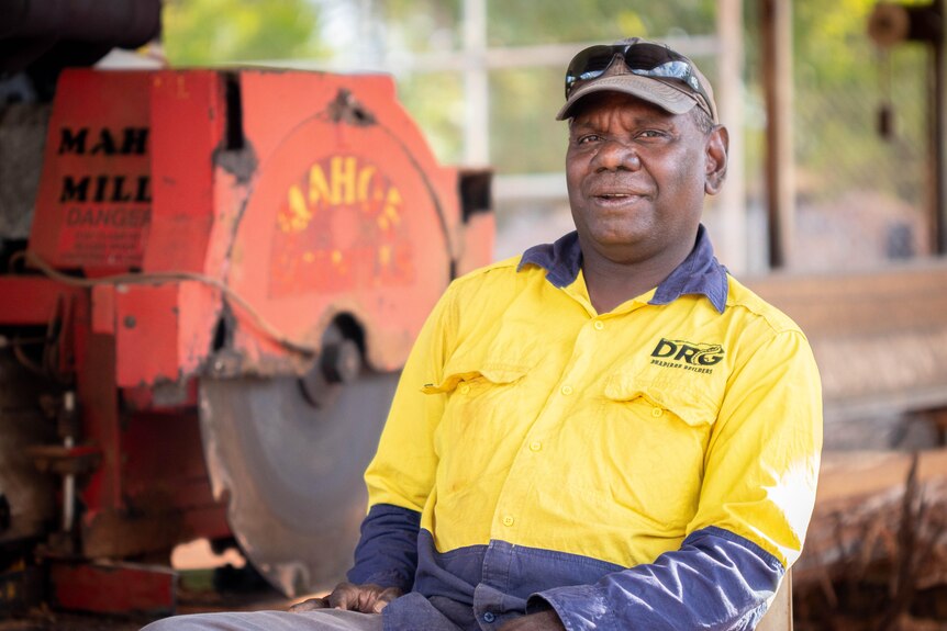 An Aboriginal man wears a high-vis shirt and stands in front of a saw mill