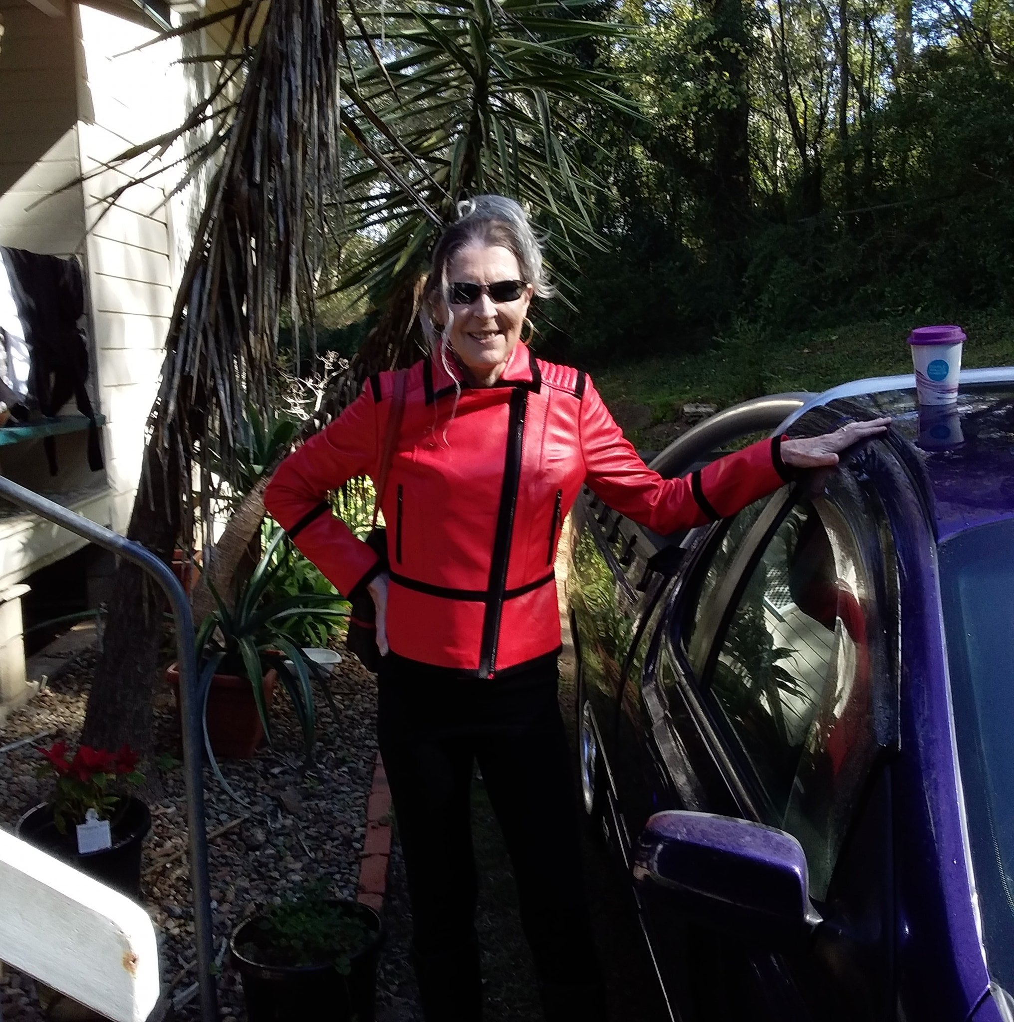 A woman in a leather jacket leans against a car.