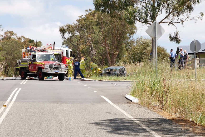 Two fire trucks sit on the side of a road as police and fire crews attend to a crashed vehicle in a ditch near a house.