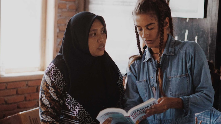 Two women, one in a headscarf, flick through a book
