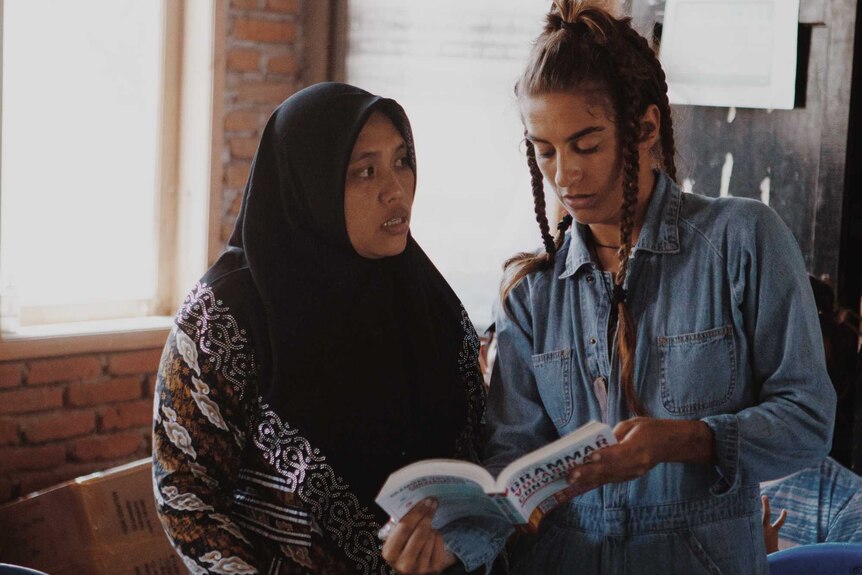Two women, one in a headscarf, flick through a book