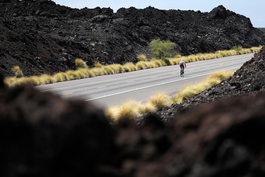 A cyclist rides up a hill with black rock on either side