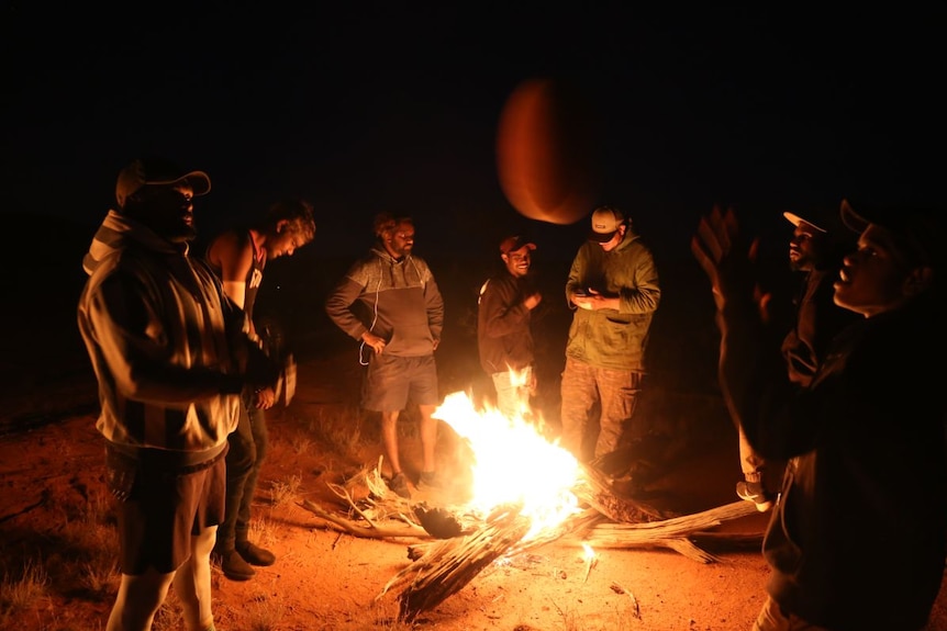 Teammates practise with a ball around a fire.