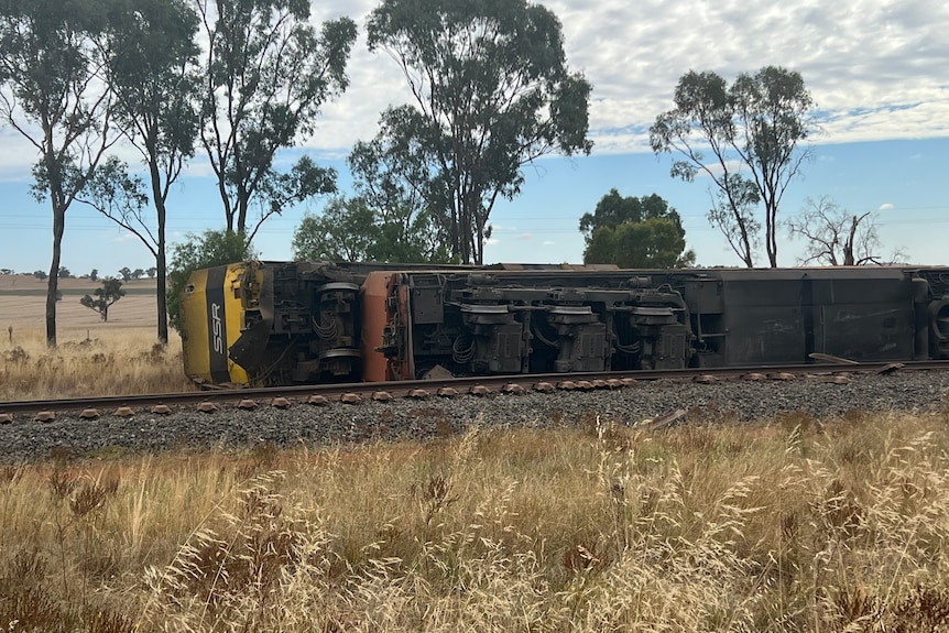 A train on its side in the country after a collision with a truck.