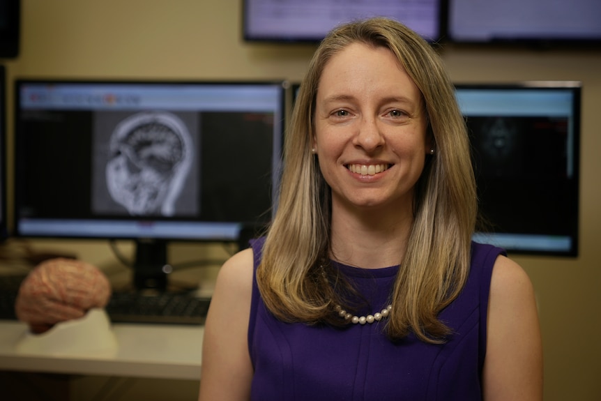 Dr Lisa Gillinder smiles in front of computers.