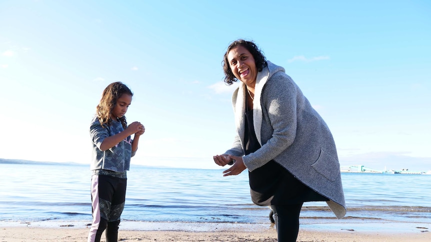 Girl on beach on left and woman on the right at beach with calm water in background