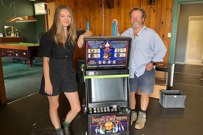 woman and man standing beside poker machine on a trolley