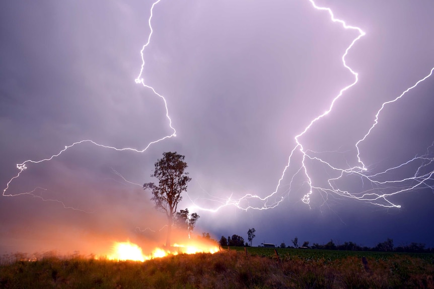 Grass fire burns as lightning arcs across sky.