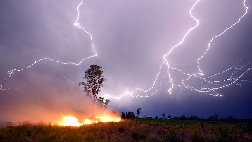 Grass fire burns as lightning arcs across sky.