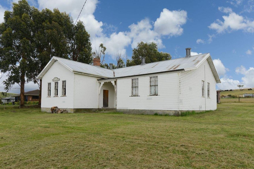 A white church building against a bush backdrop and a bright cloud-filled sky