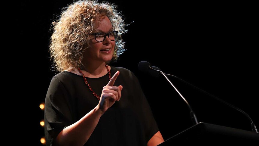 Leah Purcell wearing glasses with dark curly hair speaks at a lecturn